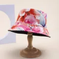 Detailed view of a reversible floral print sun bucket hat displayed on a wooden stand - 红粉紫大花卉印花