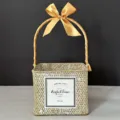 Detail view of a square hand-woven straw gift basket with an elegant golden bow handle. - Whitewashed Basket (Old Gold Ribbon)
