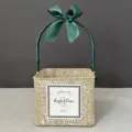 Detailed view of a square handwoven straw gift basket decorated with a green ribbon bow - White-Washed Basket [Dark Green]