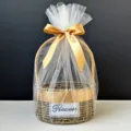 Detailed view of a round woven gift basket featuring a white tulle wrap and a gold satin ribbon - Basket With Cream Mesh And Ribbon / Champagne Gold