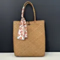 Large straw woven tote bag detail showing natural texture, floral scarf and wooden button. - Handbag + Daisy Scarf