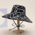 Detail view of a black and white abstract print wide-brim bucket hat with ties for summer beach. - Water Wave Black