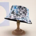 Detailed side view of a blue floral print bucket hat displayed on a classic wooden stand. - Adult 55-58cm / Blue Grey Leaf Print Style (2) / Blue Grey Leaf Print