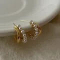 Detail van goudkleurige dubbellaagse C-vormige oorbellen met elegante witte parelaccenten - Parel Dubbellaagse Oorknopjes (R1383)