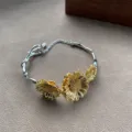 Detailopname van een zilveren en gouden zonnebloemarmband met verfijnde bloembedeltjes - Armband