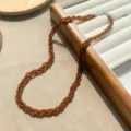 Detailansicht einer dreisträngigen bernsteinfarbenen Perlenkette auf einem Schmucktablett aus Holz - Milchtee Bernstein Halskette (ML1178) / Braun
