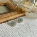 Gros plan de boucles d'oreilles fleurs sauvages argentées avec pierres vertes sur tissu - Vert (Style Aventurine Verte)