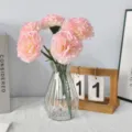 Close-up of pink artificial carnations in a faceted glass vase on a white textured desk - Pink