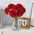 Red artificial carnations in a geometric glass vase, ideal for home table decoration. - Red