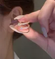 Detail view of a sparkling triple-layer gold-tone zircon ear cuff held against a human ear. - Triple Spiral Ear Cuff (R1847)