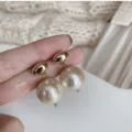 Primo piano di eleganti orecchini a bottone dorati con perle di cotone crema testurizzate - Stile Chicco d'Oro