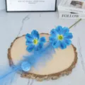 Blue artificial cosmos flower detail shot with feather decor on natural wood slice base. - Blue