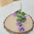 Nahaufnahme einer lila künstlichen Seidenblume mit vier Köpfen auf einer rustikalen Holzscheibe - 4-Kopf Cosmos / Lila