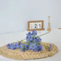 Primer plano detallado de flores artificiales de seda azul dispuestas en estera tejida. - Púrpura