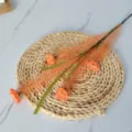 Detail view of artificial reed branches with orange flowers on a woven straw mat for home decor. - Orange
