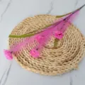 Close-up detail of artificial pink reed flower sprig on a decorative woven straw mat - Rose Red