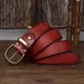 Detail view of a vintage dark red leather belt with a brass pin buckle on wood - 100cm / Red Brown
