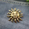 Gros plan d'une broche vintage soleil doré avec yeux en strass sur fond de denim. - Broche Soleil Style 1