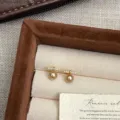 Primer plano de pendientes de perlas doradas con detalles de circonitas brillantes - Pendientes de Botón de Perla y Barra de Strass (B117)