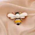 Close-up of a cute bee brooch with white enamel wings and sparkling zircon detail. - Gold Pearl Enamel Style (款式5)