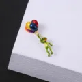 Close-up of a green cartoon frog brooch with colorful balloons on white background - Frog with Balloons
