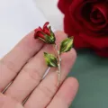 Macro detail of a vintage red rose brooch with green leaves shown held in a hand - Red Rose Style A
