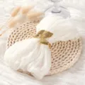 Detailopname van gouden bladvormige servietring op witte stoffen doek en geweven placemat. - 44x44cm / Wit