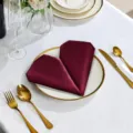 Burgundy satin dinner napkin folded in heart shape for elegant hotel table decoration and events. - Burgundy