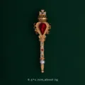 Detailed view of an ornate gold wand brooch with a vibrant red heart gemstone. - Scepter