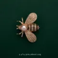 Macro view of a gold bee brooch featuring sparkling rhinestones and a large pearl. - Bee