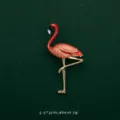 Close-up of elegant red flamingo brooch pin with gold-plated legs on green background - Flamingo