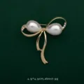 Close-up of elegant gold bow brooch with teardrop pearls and rhinestones on green background - Cloud