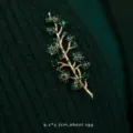 Detail view of a vintage green crystal plant branch brooch on dark green knit - Branch Leaf