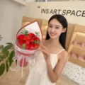 Detail view of a model holding a vibrant red soap flower bouquet with roses and lilies - Triangle Hand Bouquet / Red