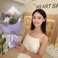 Elegant purple soap flower bouquet with roses and carnations held by a smiling woman - Triangle Hand Bouquet / Purple
