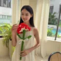Handmade crochet red carnation flower held by a smiling woman in a bright interior room - Large Single Carnation (Red) / Includes Ribbon and Gift Bag / Red