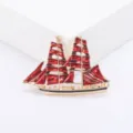 Detailed macro view of a vintage sailing ship brooch with vibrant red enamel sails - Red
