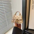 Close-up of a luxury mini monogram crossbody bag with gold-tone hardware detail. - Off White