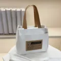 Détail d'un sac cabas en toile blanche avec anses marron et écusson en cuir pour le bureau. - Blanc