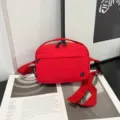 Primer plano de un bolso bandolera rojo de tela oxford impermeable sobre una revista. - Rojo