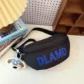 Macro view of a black nylon chest bag with blue text and a plush dog charm keychain - Black