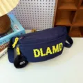 Detailed view of navy nylon chest bag with yellow DLAMD print and fuzzy eye charm - Blue