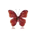 Elegante spilla a farfalla con vivaci strass rossi e arancioni su una base dorata. - Rosso