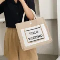 Detailed macro view of a beige linen tote bag with 'HELLO WEEKEND' slogan printing - White