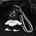 Primer plano de un llavero con forma de oso y correa de cuadros en una mochila negra. - Colgante Solo (Sin Bolso) / Panda de Lona Blanca