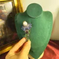 Dettaglio spilla a fiore vintage con perla e strass colorati su supporto verde. - Stile Blu Viola e Perla Bianca