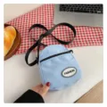 Primer plano de un bolso bandolera de nailon azul claro sobre un mantel de cuadros rojos - 7*13*16 / Azul cielo