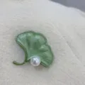 Detailed view of a green ginkgo leaf brooch with a pearl on a cream wool coat - Enamel Ginkgo Leaf (SMT1005003337135751) / Ginkgo