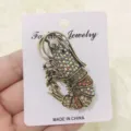 Vintage kreeftbroche met iriserende strass-steentjes op een witte sieraden displaykaart. - Koffie