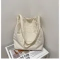 Cremefarbene Cord-Einkaufstasche mit Fashion-Label auf einem dekorativen Zeitschriftenboden - Gebrochenes Weiß